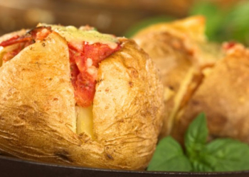 Baked potato with tomato filling and cheese on top on metal plate garnished with basil leaf (Selective Focus, Focus on the front of potato)