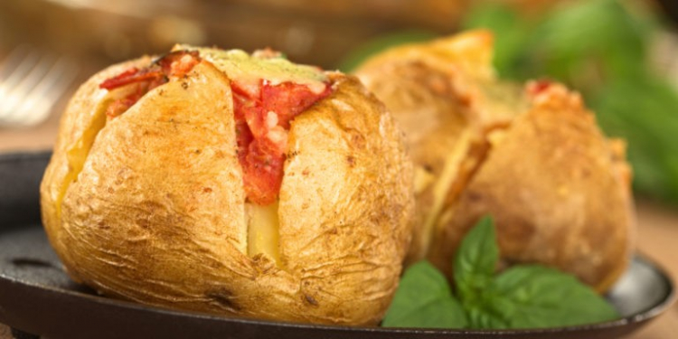 Baked potato with tomato filling and cheese on top on metal plate garnished with basil leaf (Selective Focus, Focus on the front of potato)