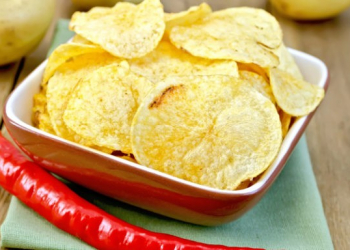 Potato chips in a clay bowl with fresh red chili peppers, fresh potatoes on the background of wooden boards