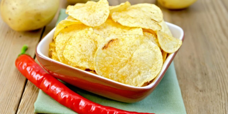 Potato chips in a clay bowl with fresh red chili peppers, fresh potatoes on the background of wooden boards