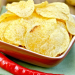 Potato chips in a clay bowl with fresh red chili peppers, fresh potatoes on the background of wooden boards