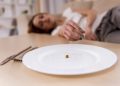 Girl exhausted from malnutrition lies on the sofa. Plate is empty side