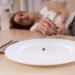 Girl exhausted from malnutrition lies on the sofa. Plate is empty side